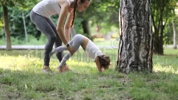 年轻的运动妈妈在绿色的夏季公园指导她的小女儿视频的预览图