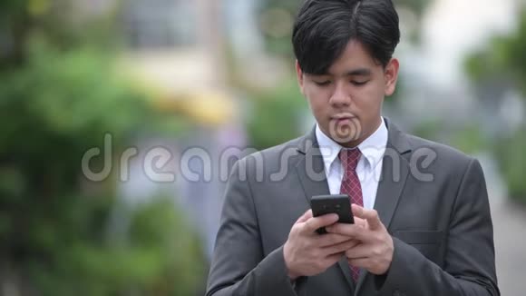 年轻英俊的亚洲商人在户外大街上用电话视频的预览图