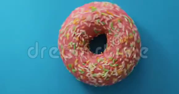 明亮而多彩的甜甜圈特写镜头旋转在蓝色背景上美味的甜甜甜面圈视频的预览图