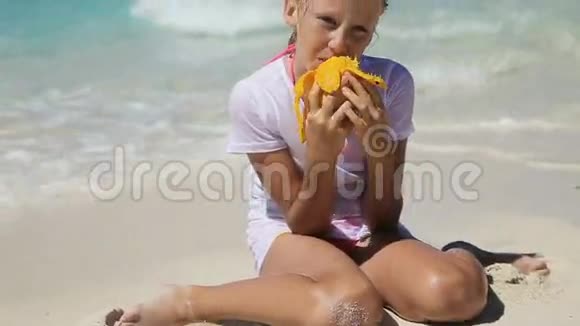 在海滩上吃芒果水果的小女孩视频的预览图