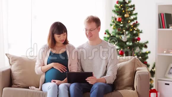 在圣诞节带平板电脑的男人和怀孕的妻子视频的预览图