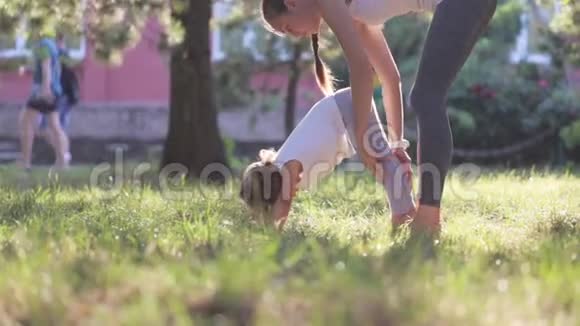 年轻的运动妈妈在绿色的夏季公园指导她的小女儿视频的预览图