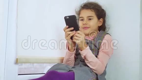 坐在窗台上玩网络智能手机的少女视频的预览图