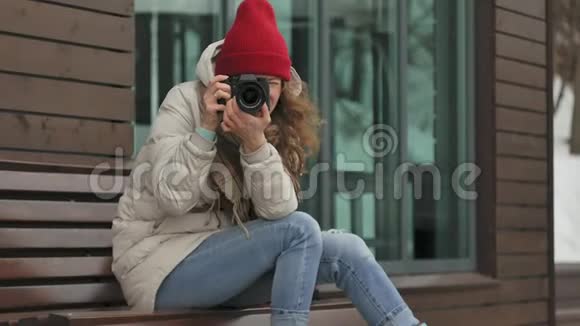 年轻漂亮的女人戴着红色帽子穿着运动温暖的衣服和滚筒坐在木凳上拿着视频的预览图