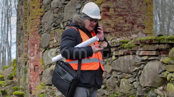 建筑检查员在旧废墟附近用智能电话交谈视频的预览图