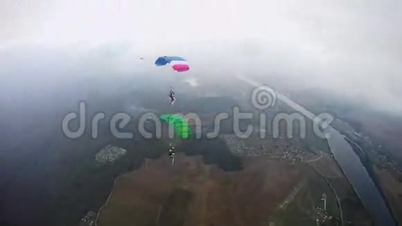 带着五颜六色降落伞的跳伞者在多云的天空中飞过绿色的田野极端极端视频的预览图