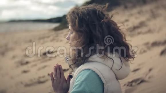 女人坐在靠近水面的沙滩上摆出一个莲花瑜伽姿势视频的预览图