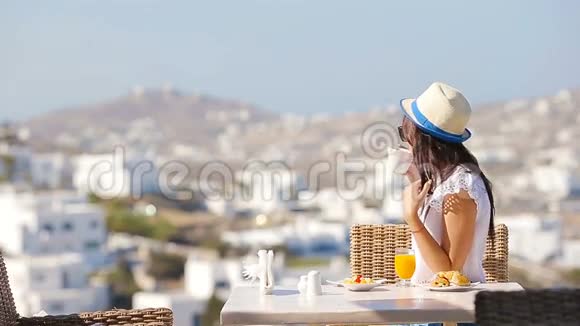 美丽优雅的女孩在户外咖啡馆吃早餐在Mykonos镇有令人惊叹的景色喝热咖啡的女人视频的预览图