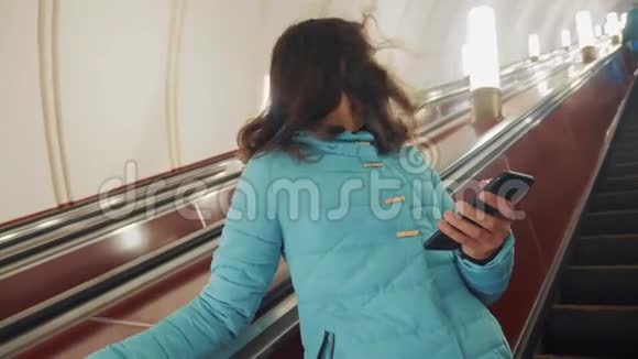 少女在地下地铁乘坐自动扶梯手持智能手机小女孩生活方式深肤色的女儿视频的预览图