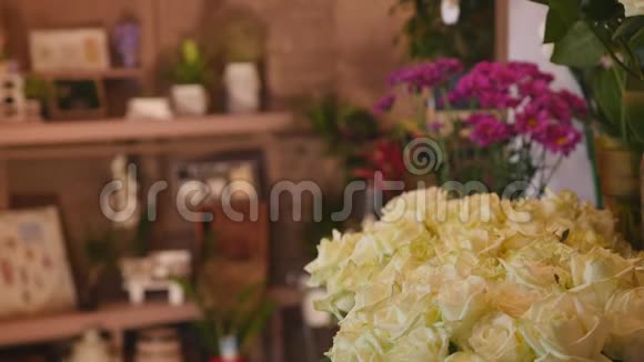 在花店里用一束束绿色的茎叶组成的白色鲜玫瑰特写镜头出售视频的预览图