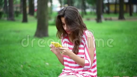漂亮的女人坐在公园的长凳上拿着智能手机视频的预览图