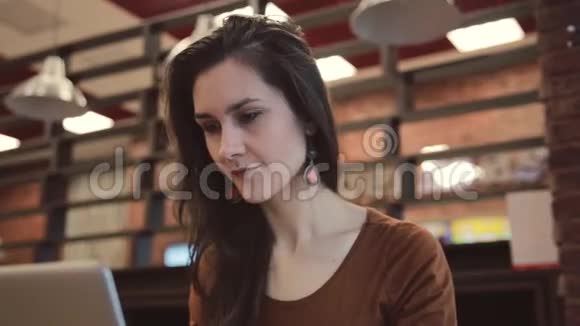 年轻的黑发女孩在咖啡馆里用笔记本电脑工作视频的预览图