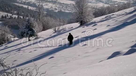 一个孤独的游客走过山林中的雪冬天雪林里的旅行者一个年轻人视频的预览图