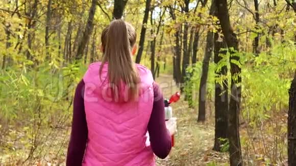 美丽的健身运动女孩走在秋季公园的运动服与运动水瓶或等渗饮料在手视频的预览图