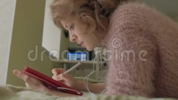 快乐的女孩听音乐用手写笔在家里的卧室里用平板电脑画画网上冲浪远程工作视频的预览图