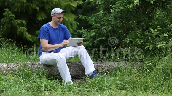 一个带着平板电脑的人坐在森林里一棵倒下的树上视频的预览图