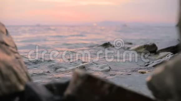 特写慢动作低角度小海浪在岩石海滩上翻滚海边傍晚在卵石岩石海滩上日落视频的预览图