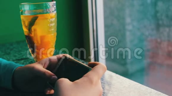 一个男孩在柠檬茶和肉桂旁边的咖啡馆玩智能手机视频的预览图