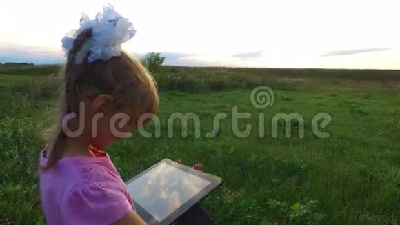 小女孩热情地在平板电脑上玩戴眼镜的女孩子站在绿色的草地上视频的预览图