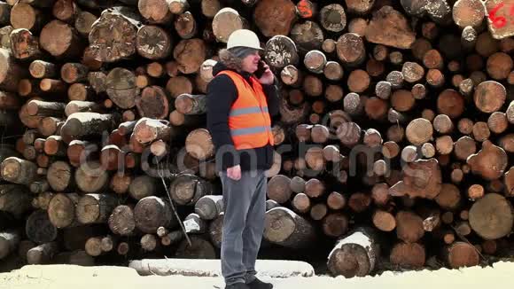 冬天工程师在靠近成堆原木的智能手机上讲话视频的预览图