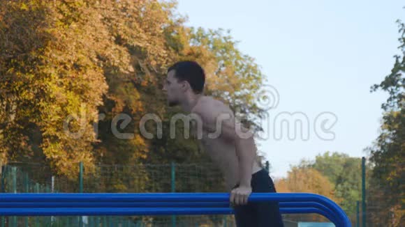 在城市公园的运动场运动员在双杠上做俯卧撑强壮的年轻肌肉男在户外训练视频的预览图
