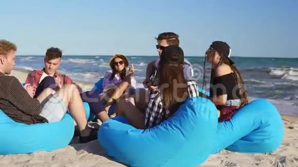 一群朋友坐在沙滩上的安乐椅上弹吉他在夏天的晚上唱歌慢镜头视频的预览图