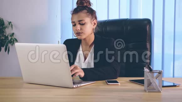 女孩穿着时尚的衣服坐在办公室里在笔记本电脑上打印信息视频的预览图
