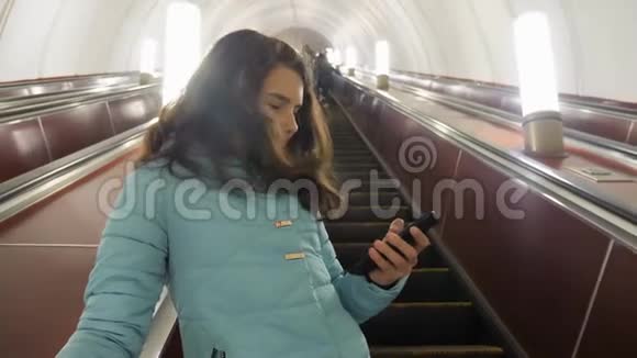 少女在地下地铁乘坐自动扶梯手持智能手机小女孩黑发女儿搜索视频的预览图