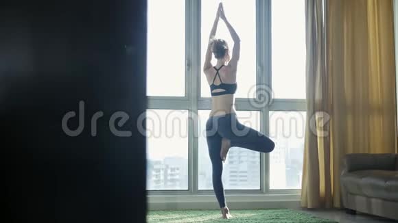 有城市景观背景的年轻女性在家练习瑜伽视频的预览图