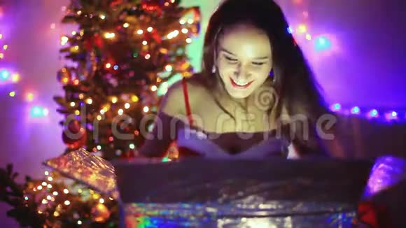 年轻快乐的女人坐在圣诞树旁边装饰着神奇的圣诞礼物1920x1080视频的预览图