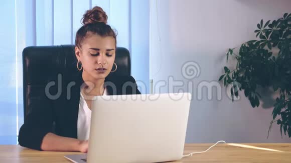 女孩穿着时尚的衣服坐在办公室里在笔记本电脑上打印信息视频的预览图