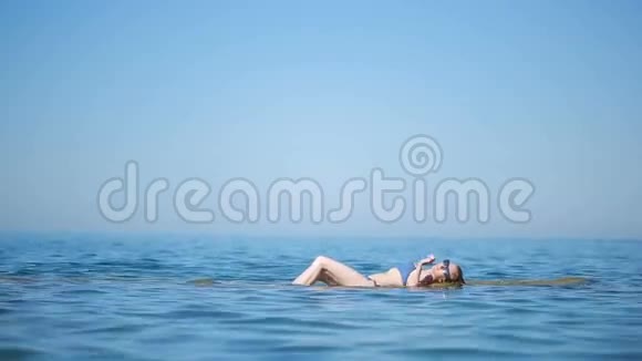穿着蓝色比基尼的女孩在海浪中躺在海滩上玩得很开心视频的预览图