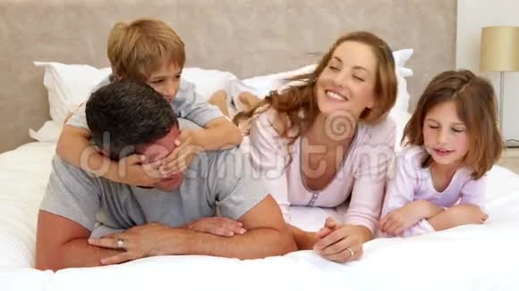 可爱的父母和孩子躺在床上开玩笑视频的预览图
