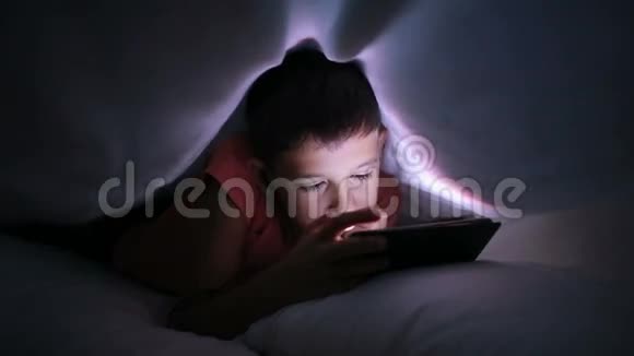 小男孩在床上玩手机或智能手机夜晚视频的预览图