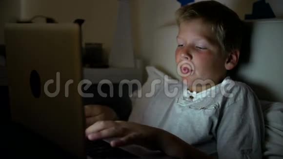 夜间在床上使用笔记本电脑的男孩视频的预览图