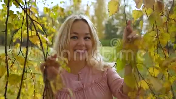 年轻漂亮的金发女郎在一个带有黄昏灯光的秋天公园的背景下慢动作视频的预览图