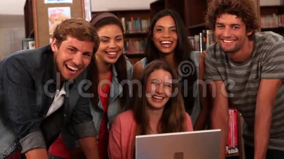 快乐的学生拿着笔记本电脑站在图书馆视频的预览图
