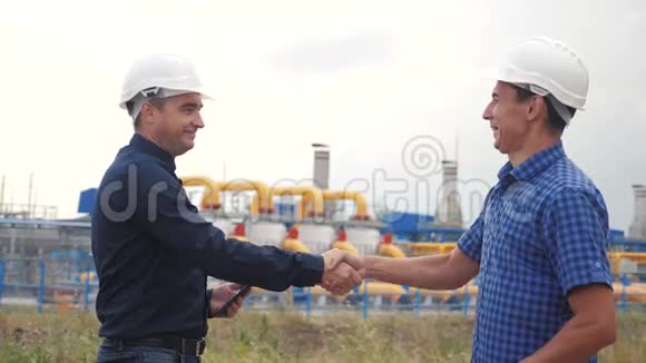 团队合作工业煤气生产站的概念慢动作录像两名戴头盔的工程师在天然气上握手视频的预览图