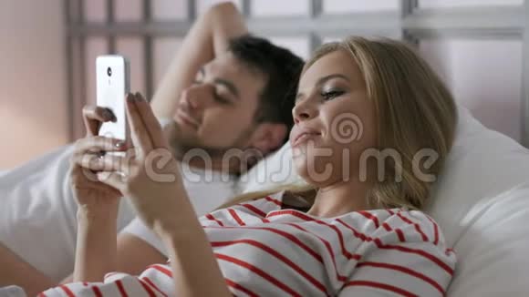 年轻家庭在卧室里用手机上网视频的预览图