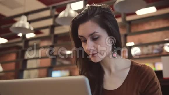 年轻的黑发女孩在咖啡馆里用笔记本电脑工作视频的预览图