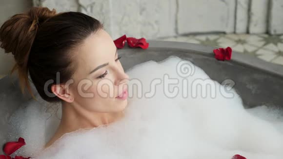女孩躺在泡沫的大石头浴室里视频的预览图