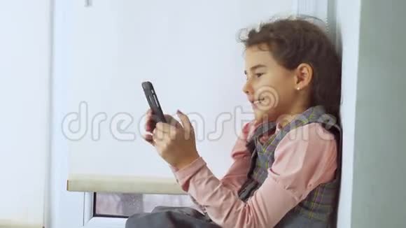 坐在网上窗台上玩智能手机网络游戏的少女视频的预览图