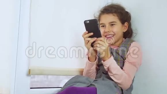 坐在窗台上玩智能手机网络游戏的少女视频的预览图