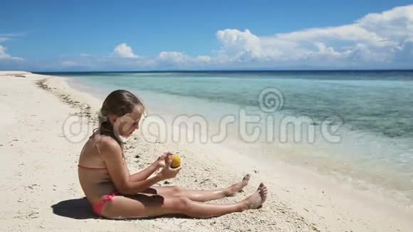 在海滩上吃芒果水果的小女孩视频的预览图