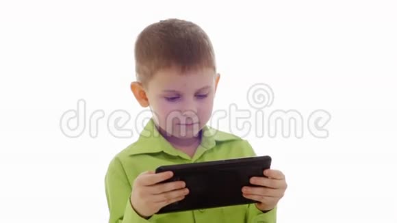 穿绿色衬衫的孩子正坐在床上玩平板电脑视频的预览图
