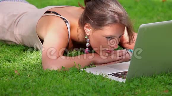 快乐的学生躺在草地上看着笔记本电脑视频的预览图