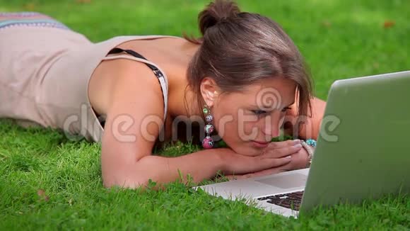 微笑的学生躺在草地上看着笔记本电脑视频的预览图