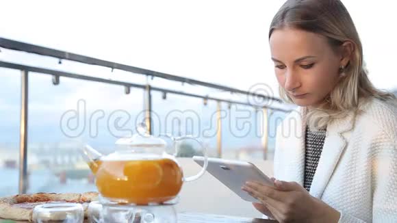 坐在咖啡馆里的年轻漂亮的女士带着平板电脑视频的预览图