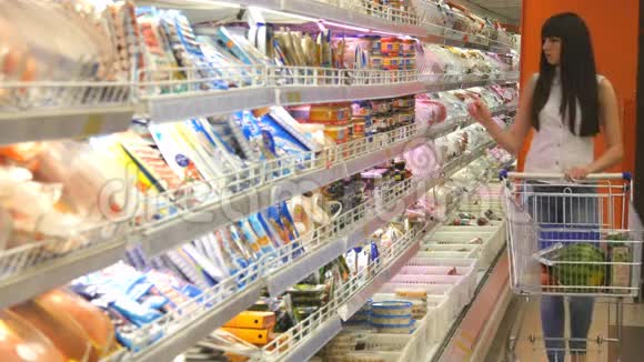 带着购物车在冷藏区的超市里买奶制品或冷藏食品的年轻女子视频的预览图