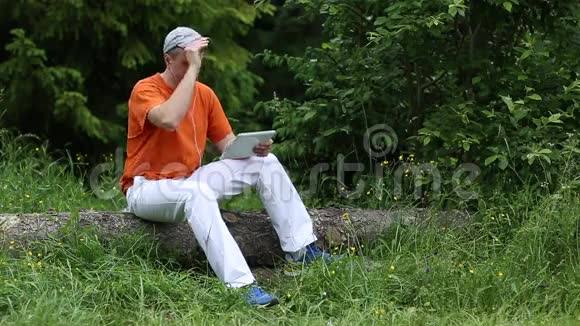 一个带着平板电脑的人坐在森林里一棵倒下的树上视频的预览图